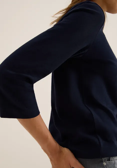 Frau mit dunkelblauem Langarmshirt und Jeans, seitlich aufgenommen.